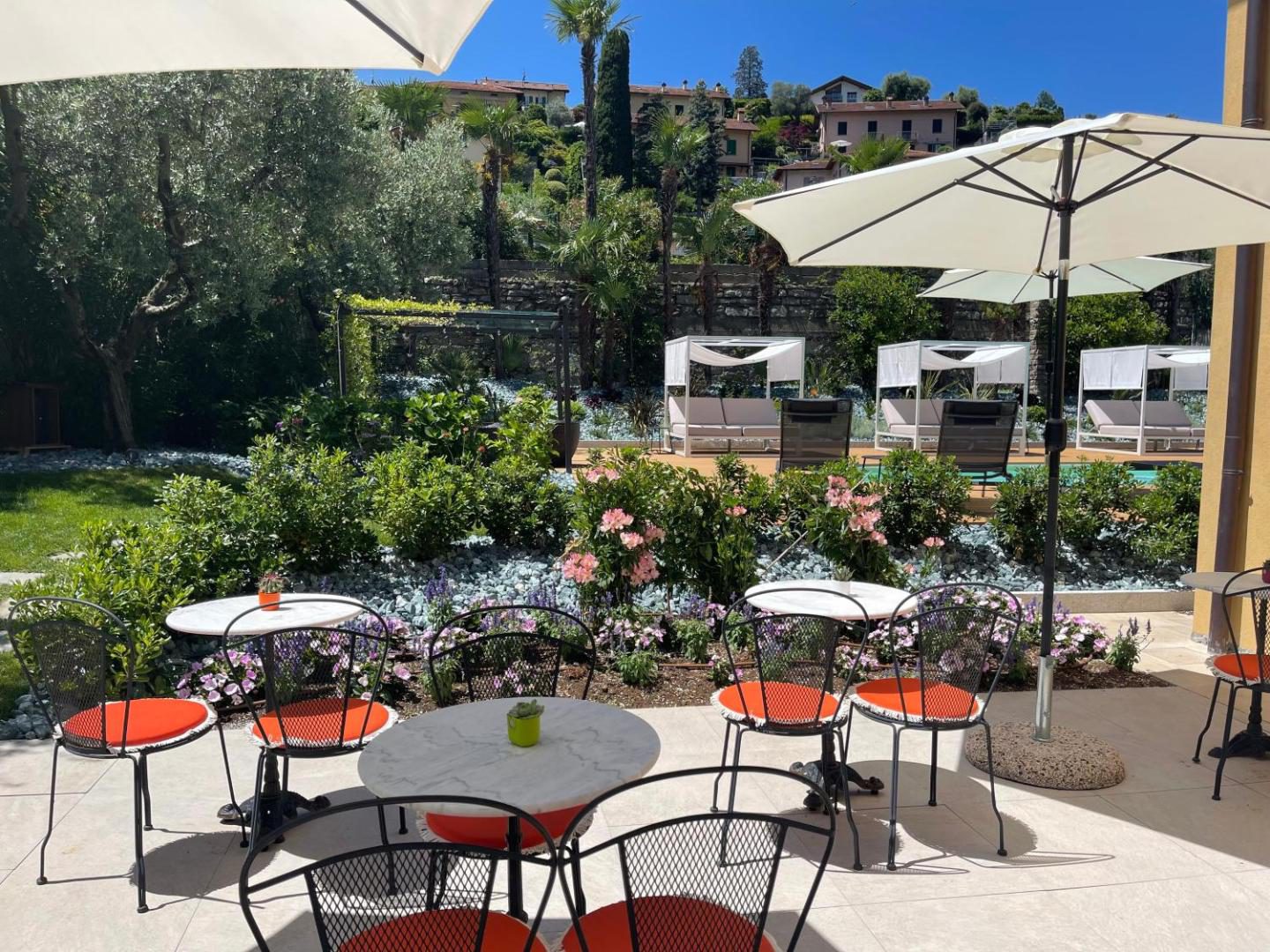 Charming Bellagio Boutique Hotel – terasa cu mese rotunde si scaune portocalii, gradina cu flori si piscina vizibila in fundal, Bellagio Charming Bellagio Boutique Hotel – terasa cu mese rotunde si scaune portocalii, gradina cu flori si piscina vizibila in fundal, Bellagio
