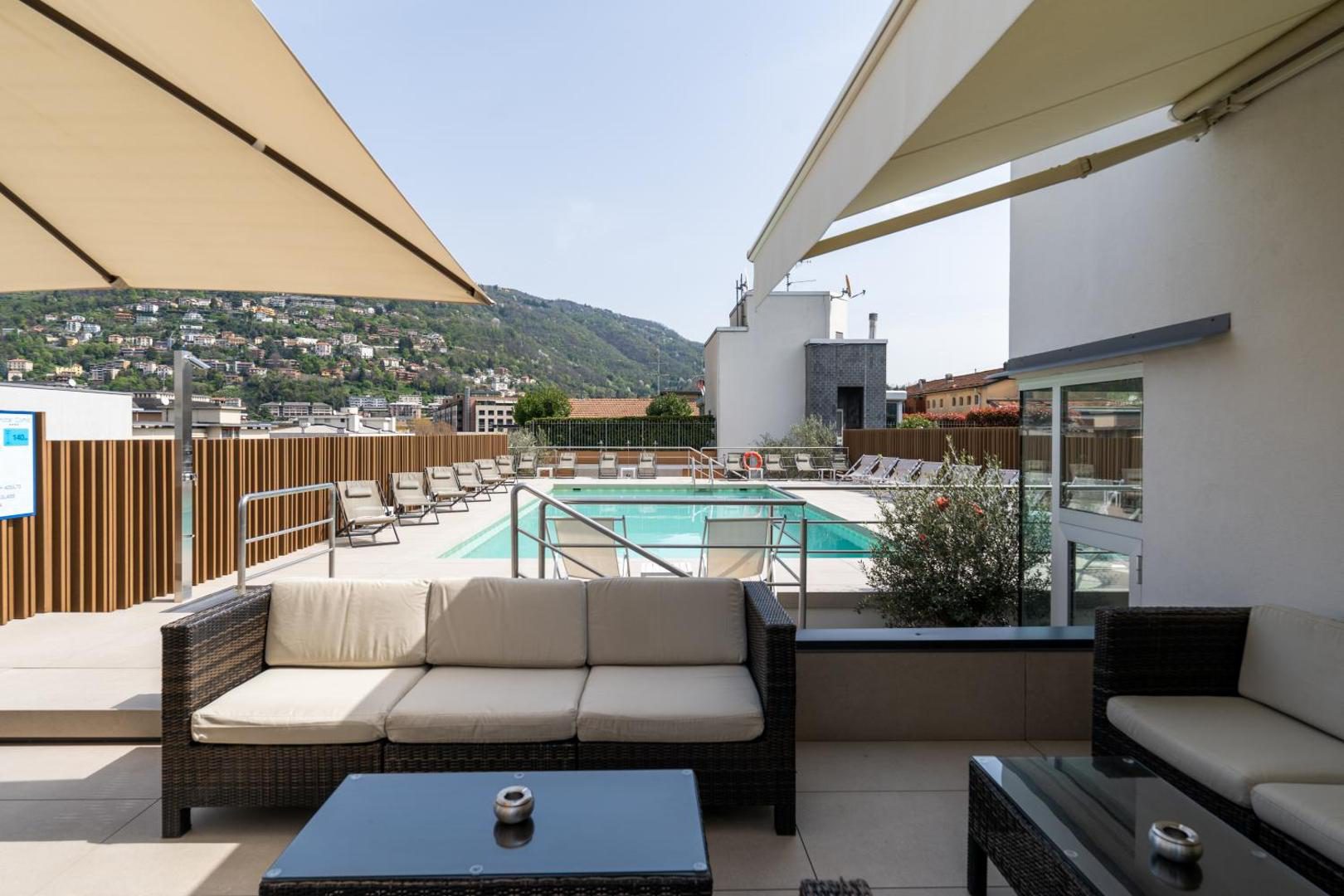 Hotel Como – terasa pe acoperis cu canapele rattan, sezlonguri si piscina, cu munti in fundal Hotel Como – terasa pe acoperis cu canapele rattan, sezlonguri si piscina, cu munti in fundal