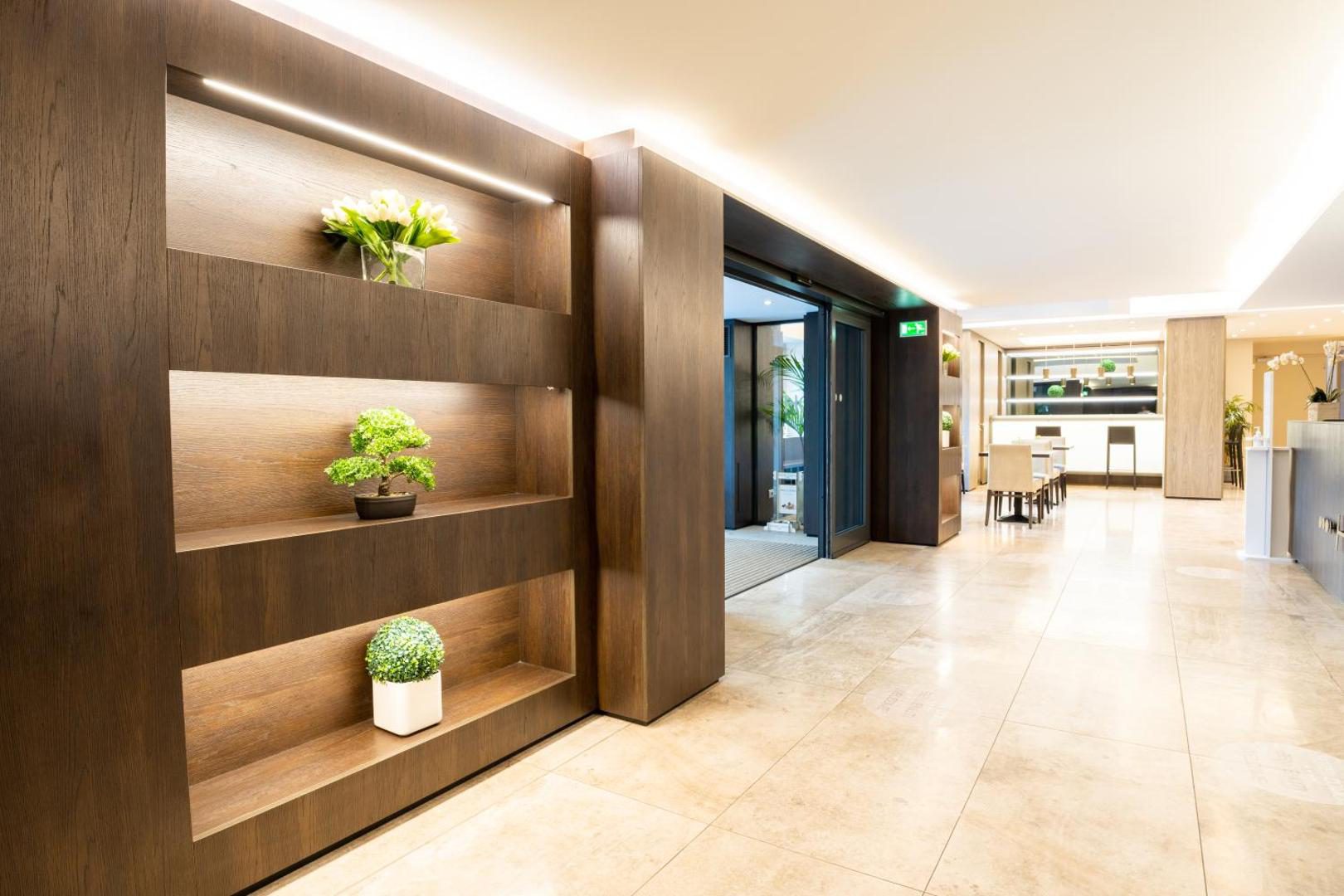 Hotel Como – hol elegant cu rafturi din lemn cu plante, podea din marmura si zona de restaurant Hotel Como – hol elegant cu rafturi din lemn cu plante, podea din marmura si zona de restaurant
