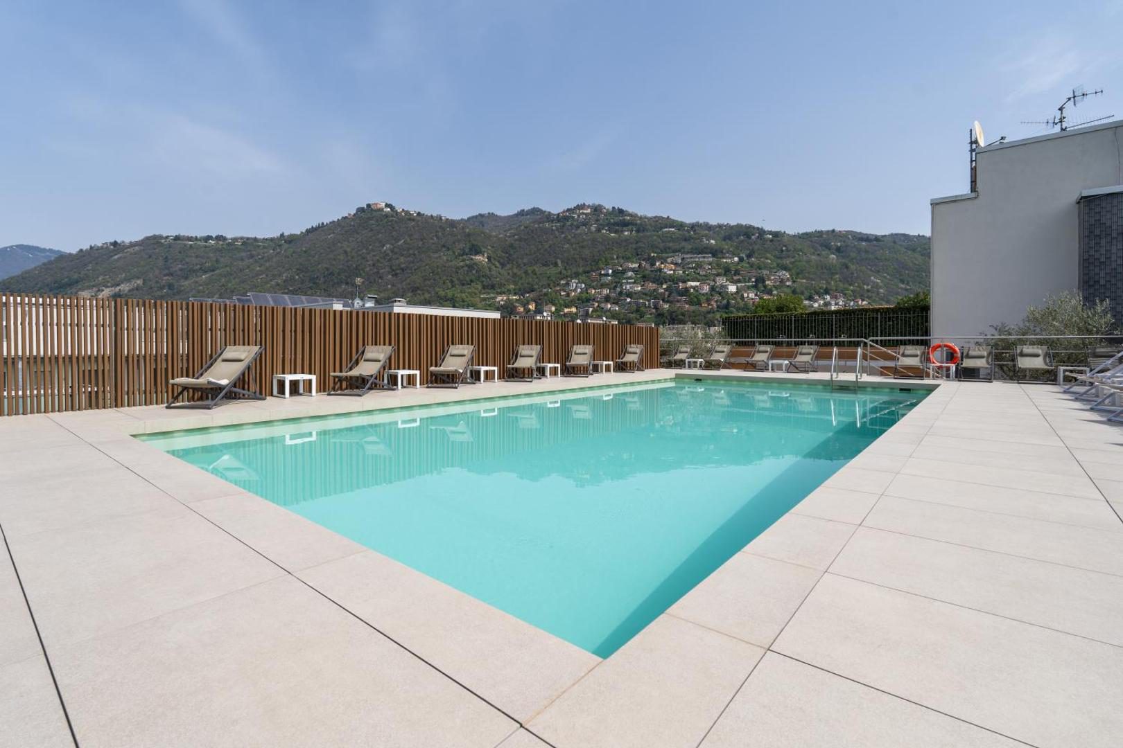 Hotel Como – piscina pe acoperis cu sezlonguri si vedere la dealurile verzi din Como Hotel Como – piscina pe acoperis cu sezlonguri si vedere la dealurile verzi din Como