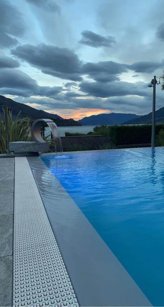 Hotel Domaso – piscina în aer liber seara cu cascadă ornamentală și vedere la lac la apus Hotel Domaso – piscina în aer liber seara cu cascadă ornamentală și vedere la lac la apus