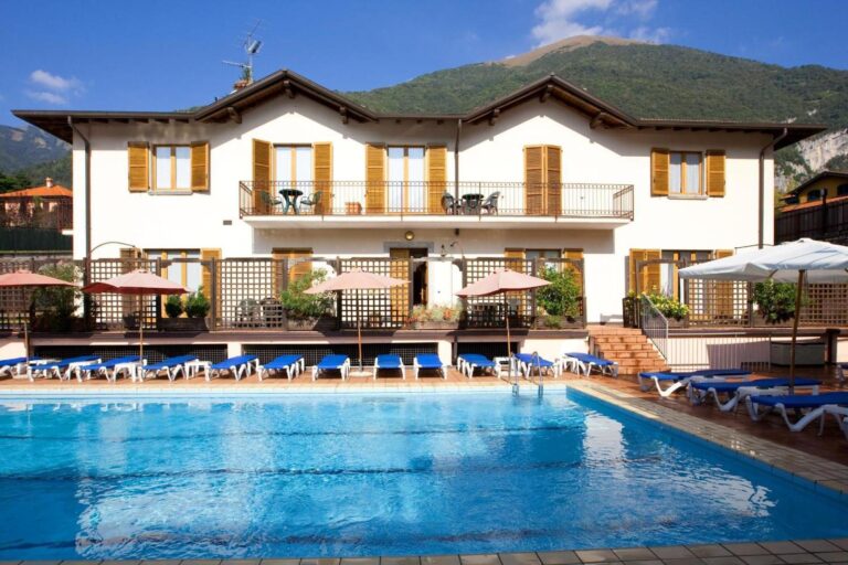 Hotel Lenno – piscina exterioara sezoniera cu sezlonguri albastre si umbrele, hotel cu obloane de lemn in fundal si munti, Lenno, Lacul Como