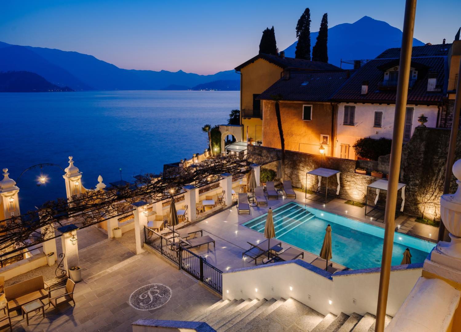 Hotel Royal Victoria Varenna – piscina incalzita iluminata la amurg cu vedere la Lacul Como si munti, terasa cu sezlonguri si pergola, Varenna Hotel Royal Victoria Varenna – piscina incalzita iluminata la amurg cu vedere la Lacul Como si munti, terasa cu sezlonguri si pergola, Varenna