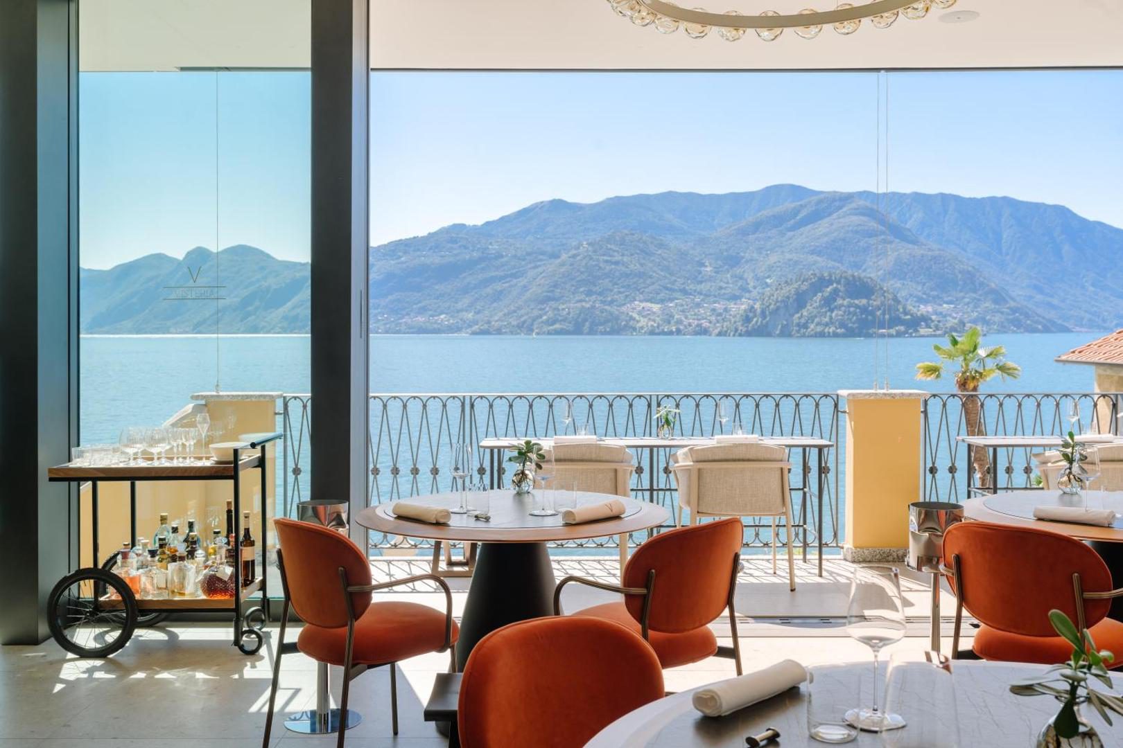 Hotel Royal Victoria Varenna – restaurantul Visteria cu pereti de sticla panoramici cu vedere la Lacul Como, mese cu scaune portocalii, Varenna Hotel Royal Victoria Varenna – restaurantul Visteria cu pereti de sticla panoramici cu vedere la Lacul Como, mese cu scaune portocalii, Varenna
