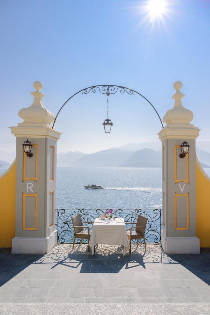 Hotel Royal Victoria Varenna – poarta neoclasica galbena cu coloane monogram R V si masa romantica pentru doi cu Lacul Como in fundal, Varenna Hotel Royal Victoria Varenna – poarta neoclasica galbena cu coloane monogram R V si masa romantica pentru doi cu Lacul Como in fundal, Varenna