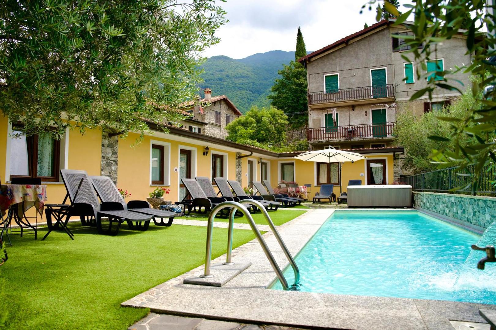 Hotel Diffuso Il Portichetto Perledo – piscina exterioara sezoniera cu sezlonguri si umbrela, gradina verde si cladirile vilei in fundal, Perledo, Lacul Como Hotel Diffuso Il Portichetto Perledo – piscina exterioara sezoniera cu sezlonguri si umbrela, gradina verde si cladirile vilei in fundal, Perledo, Lacul Como
