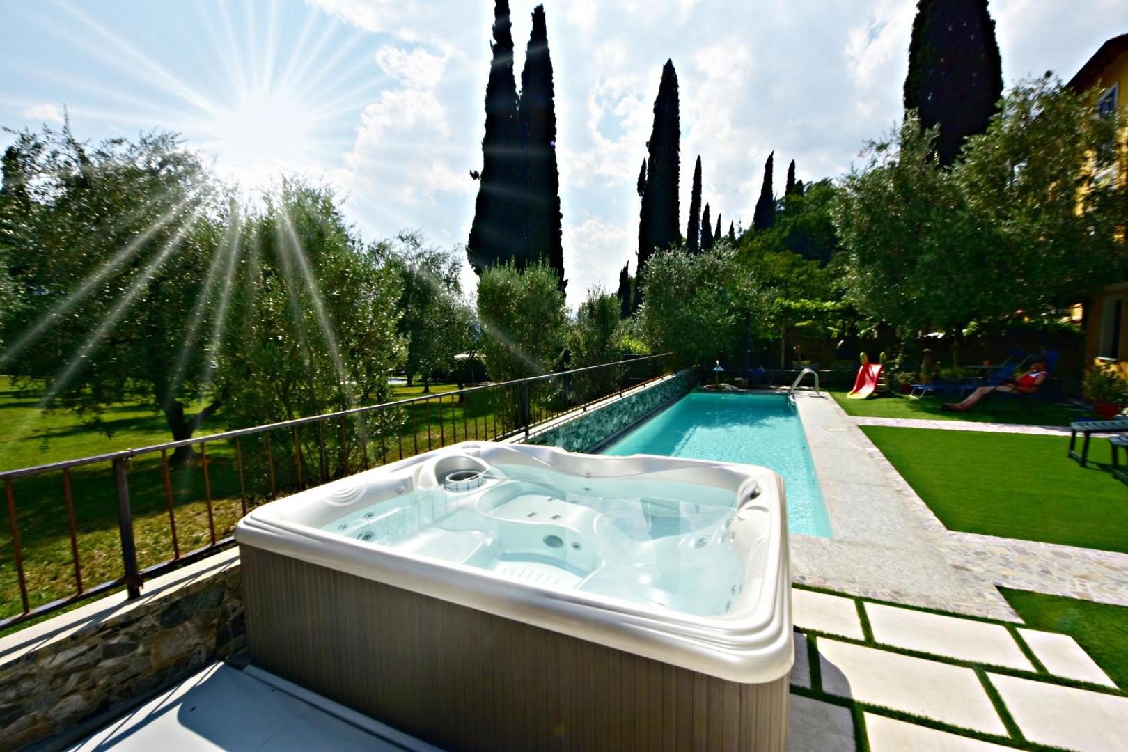 Hotel Diffuso Il Portichetto Perledo – jacuzzi exterior pe terasa de piatra, piscina sezoniera si gradina cu chiparosi in fundal sub raze de soare, Perledo, Lacul Como Hotel Diffuso Il Portichetto Perledo – jacuzzi exterior pe terasa de piatra, piscina sezoniera si gradina cu chiparosi in fundal sub raze de soare, Perledo, Lacul Como