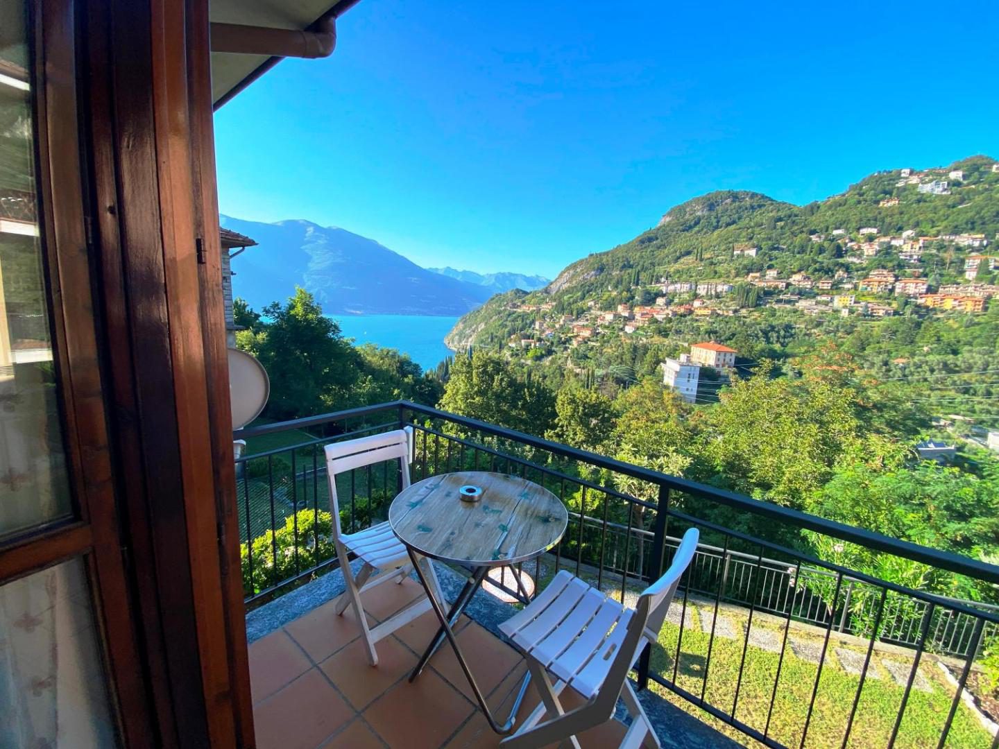 Hotel Diffuso Il Portichetto Perledo – balcon cu masa rotunda si scaune albe cu vedere panoramica la Lacul Como, sate pe maluri si munti verzi, Perledo Hotel Diffuso Il Portichetto Perledo – balcon cu masa rotunda si scaune albe cu vedere panoramica la Lacul Como, sate pe maluri si munti verzi, Perledo