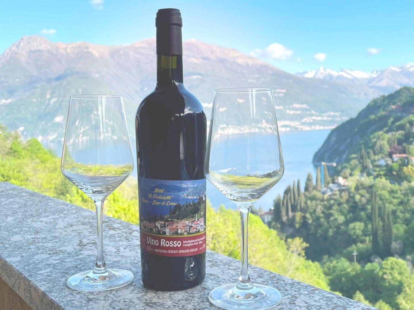 Hotel Diffuso Il Portichetto Perledo – sticla de Vino Rosso al hotelului si doua pahare pe balustrada cu panorama Lacul Como si Varenna in fundal, Perledo Hotel Diffuso Il Portichetto Perledo – sticla de Vino Rosso al hotelului si doua pahare pe balustrada cu panorama Lacul Como si Varenna in fundal, Perledo