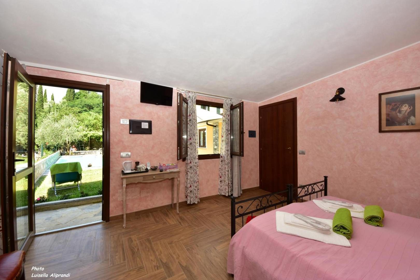 Hotel Diffuso Il Portichetto Perledo – camera cu peretii roz, pat cu cadru de fier, usa spre terasa si gradina cu piscina vizibila, Perledo, Lacul Como Hotel Diffuso Il Portichetto Perledo – camera cu peretii roz, pat cu cadru de fier, usa spre terasa si gradina cu piscina vizibila, Perledo, Lacul Como