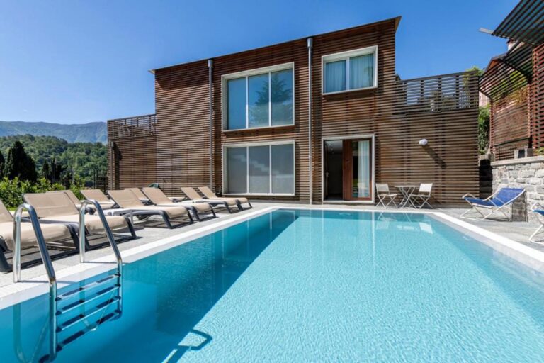 Residence Lenno – piscina infinita exterioara cu sezlonguri, cladire cu lamele din lemn in fundal si munti Alpi, Lenno, Lacul Como