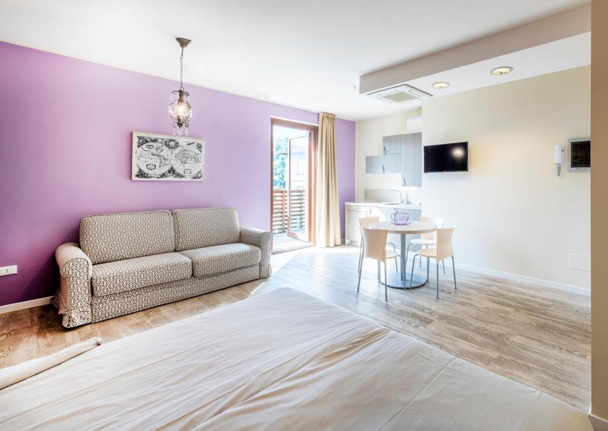 Residence Lenno – studio cu perete mov, canapea extensibila, masa dining si bucatarie, cu usa spre balcon cu vedere la munte, Lenno Residence Lenno – studio cu perete mov, canapea extensibila, masa dining si bucatarie, cu usa spre balcon cu vedere la munte, Lenno