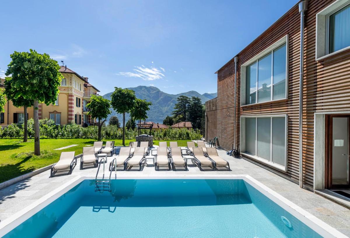 Residence Lenno – piscina exterioara cu gradina verde, copaci si munti in fundal, cladire moderna cu fatada din lemn, Lenno Residence Lenno – piscina exterioara cu gradina verde, copaci si munti in fundal, cladire moderna cu fatada din lemn, Lenno