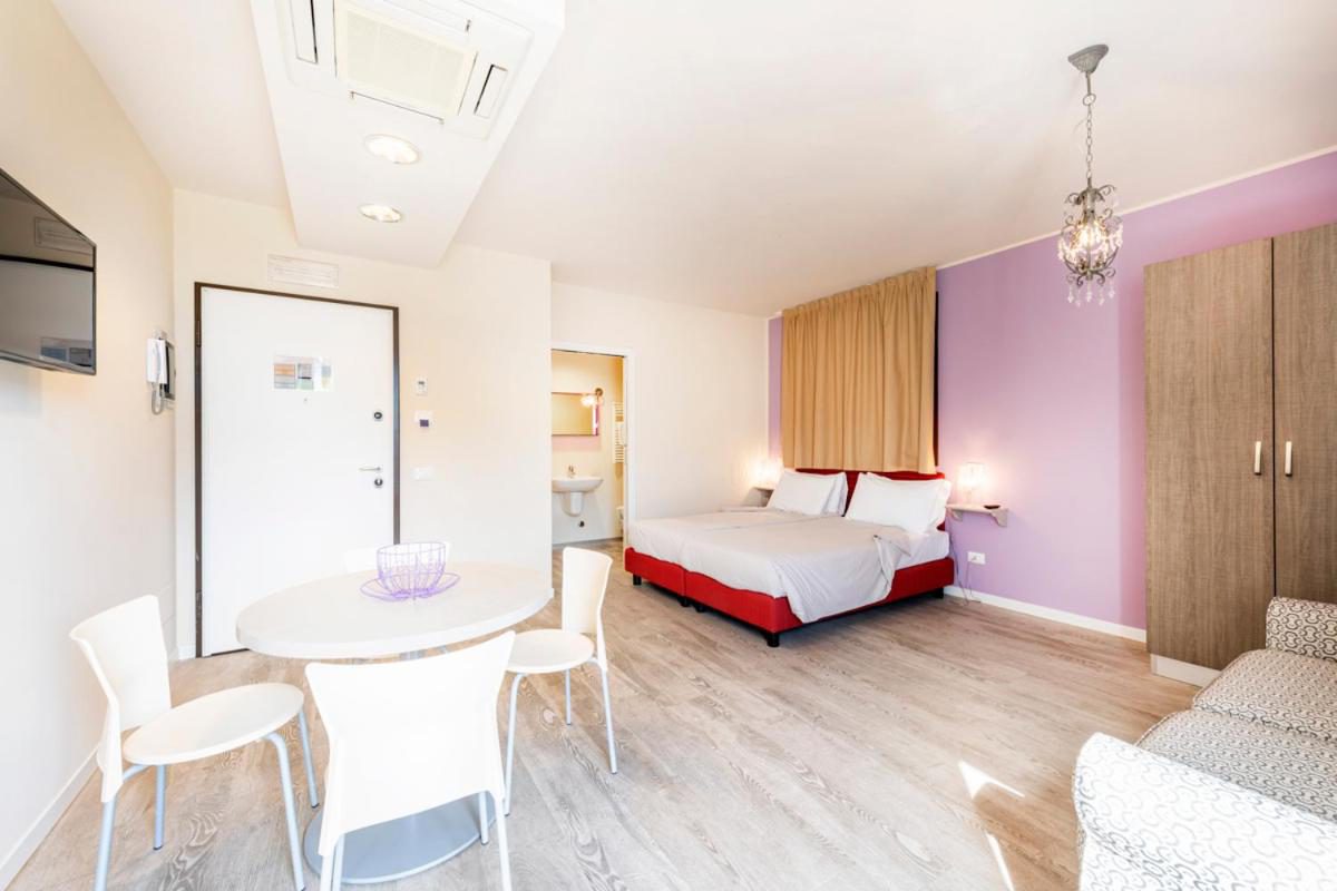 Residence Lenno – studio open plan cu pat dublu, masa dining alba si bucatarie, perete roz/mov, Lenno Residence Lenno – studio open plan cu pat dublu, masa dining alba si bucatarie, perete roz/mov, Lenno