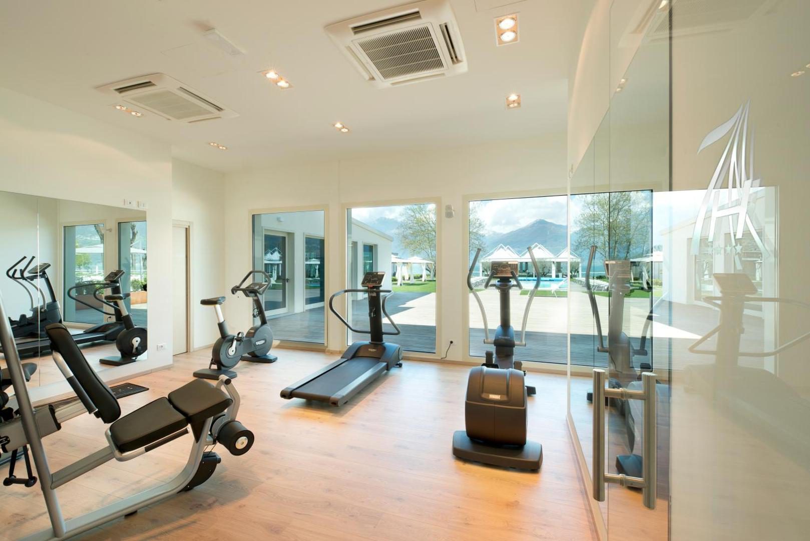 Seven Park Hotel – sala de fitness moderna cu echipamente si pereti de sticla cu vedere la piscina si munti, Colico Seven Park Hotel – sala de fitness moderna cu echipamente si pereti de sticla cu vedere la piscina si munti, Colico