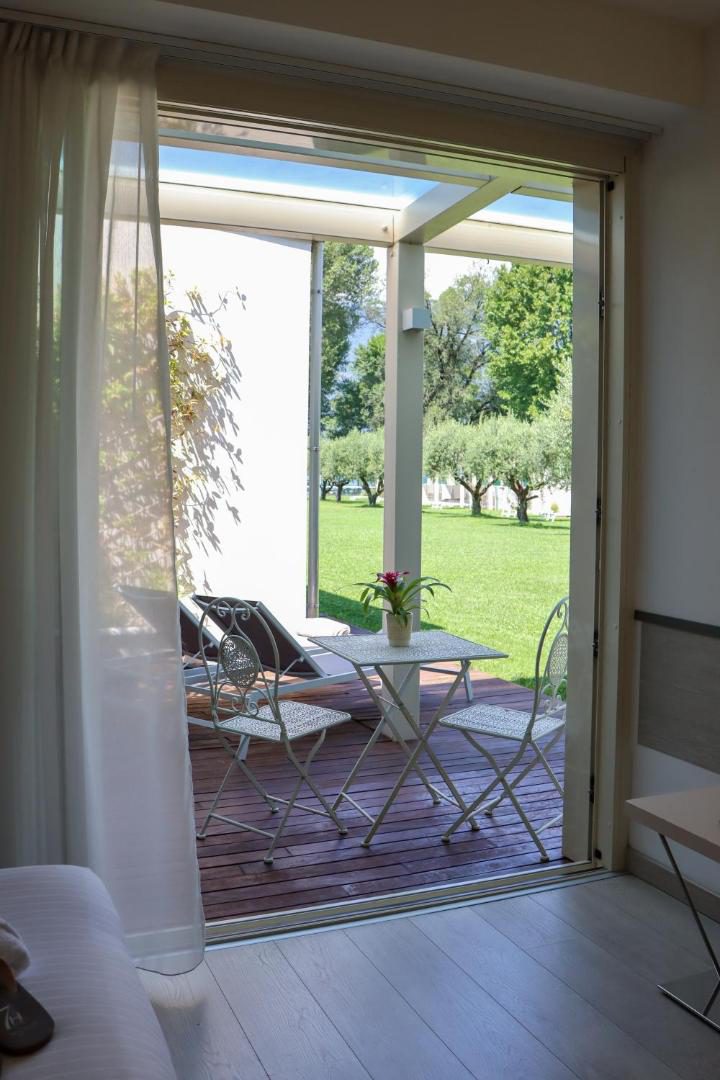 Seven Park Hotel – terasa privata cu mobilier din fier forjat alb pe deck din lemn, cu vedere la gradina cu maslin, Colico Seven Park Hotel – terasa privata cu mobilier din fier forjat alb pe deck din lemn, cu vedere la gradina cu maslin, Colico