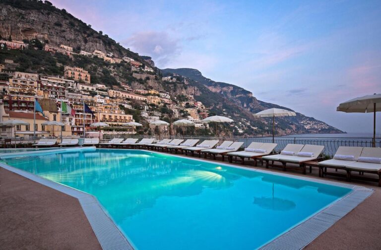 Covo dei Saraceni Positano – piscina infinity iluminata la amurg cu sezlonguri si prosoape albe, vedere la orasul Positano si mare, Coasta Amalfitana