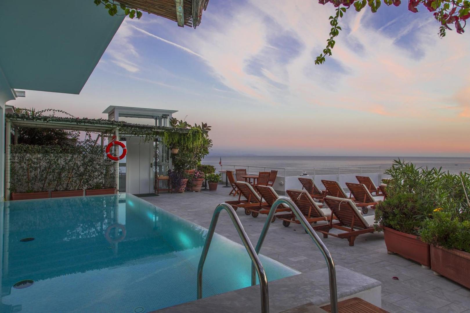 Hotel Marina Riviera Amalfi – piscina pe acoperis la apus, sezlonguri din lemn si vedere panoramica la mare Hotel Marina Riviera Amalfi – piscina pe acoperis la apus, sezlonguri din lemn si vedere panoramica la mare