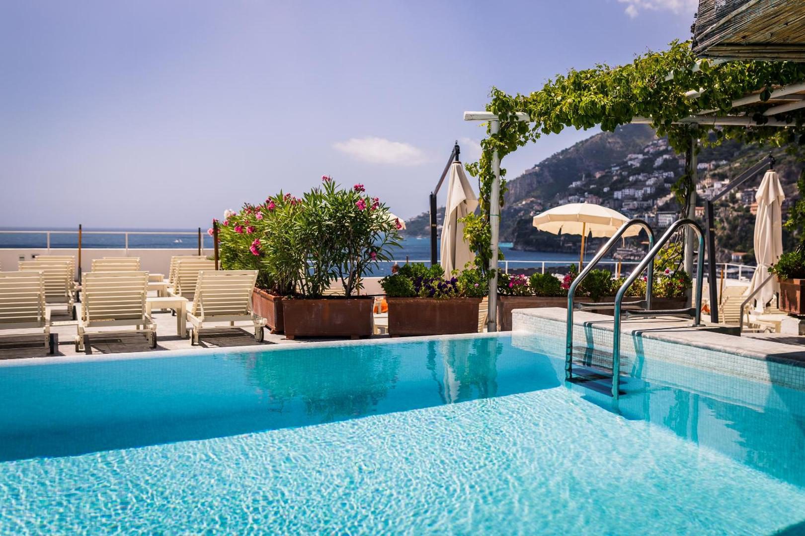 Hotel Marina Riviera Amalfi – piscina rooftop cu sezlonguri, oleandri roz si vedere la mare Hotel Marina Riviera Amalfi – piscina rooftop cu sezlonguri, oleandri roz si vedere la mare