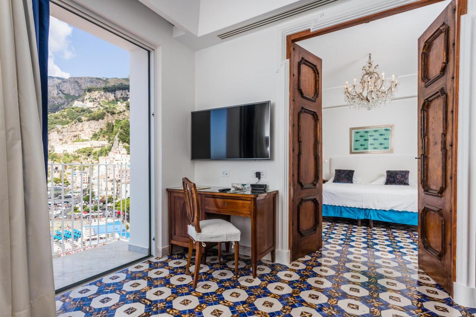 Hotel Marina Riviera Amalfi – dormitor cu usi din lemn masiv, candelabru de cristal si vedere la orasul Amalfi Hotel Marina Riviera Amalfi – dormitor cu usi din lemn masiv, candelabru de cristal si vedere la orasul Amalfi