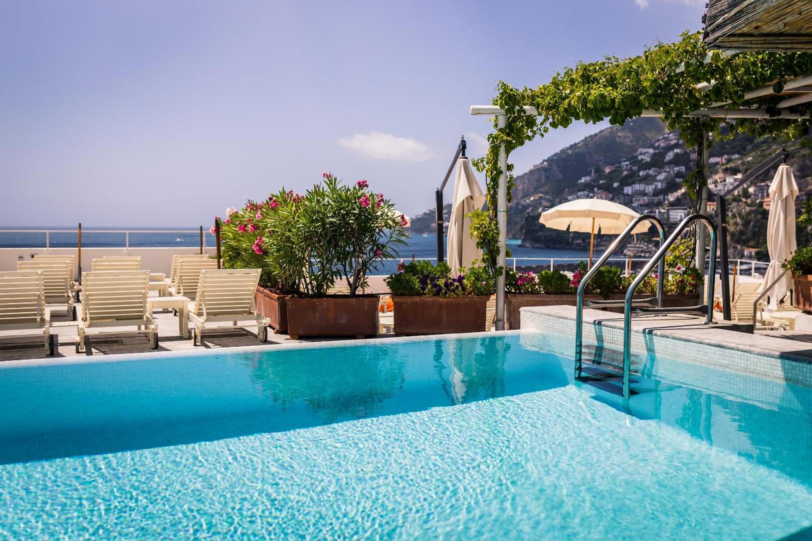 Hotel Marina Riviera Amalfi – piscina rooftop ziua cu apa turcoaz, pergola cu vita de vie si vedere la coasta Hotel Marina Riviera Amalfi – piscina rooftop ziua cu apa turcoaz, pergola cu vita de vie si vedere la coasta