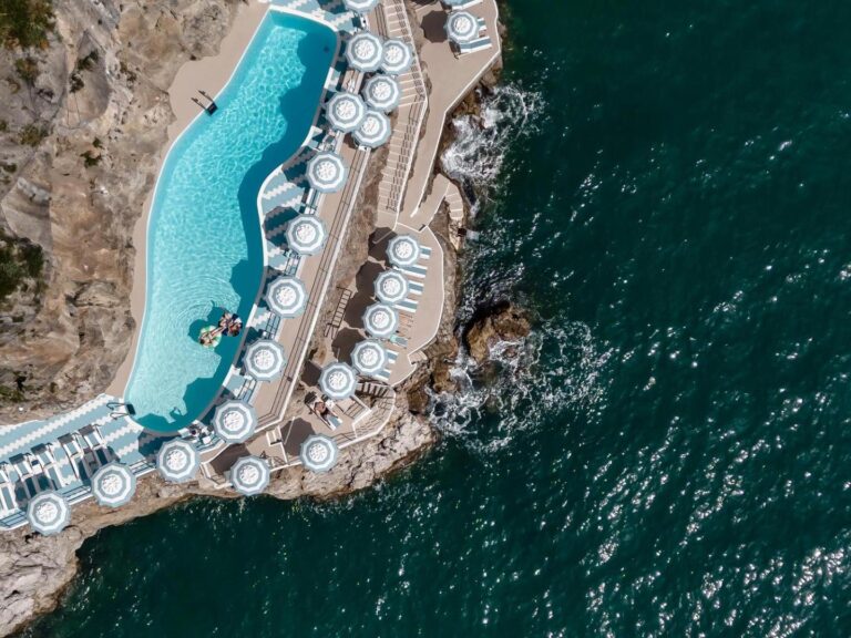 Hotel Miramalfi Amalfi – piscina sapata in stanca vazuta din avion, sezlonguri si umbrele albastru-alb, valuri pe stanci