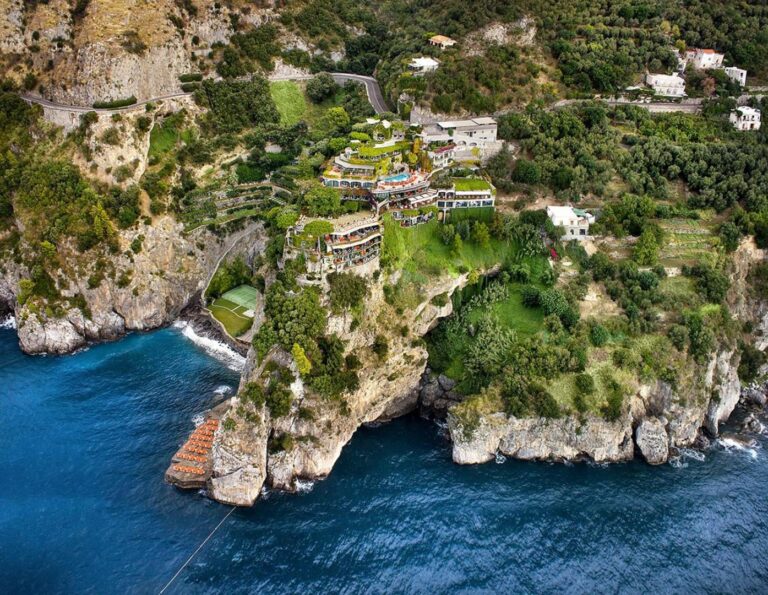 Il San Pietro di Positano – vedere aeriana a hotelului construit in terase pe stanca, cu piscina exterioara, teren de tenis si plaja privata la baza stancii, Positano