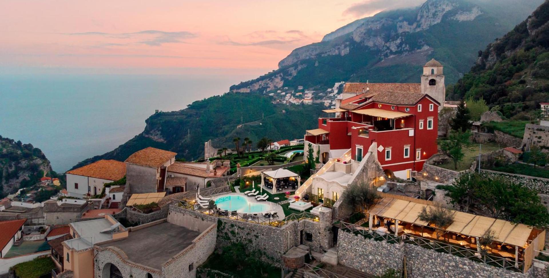 Palazzo Pascal Scala – vedere aeriana la asfintit asupra palatului rosu si piscinei, cu Coasta Amalfitana in fundal Palazzo Pascal Scala – vedere aeriana la asfintit asupra palatului rosu si piscinei, cu Coasta Amalfitana in fundal