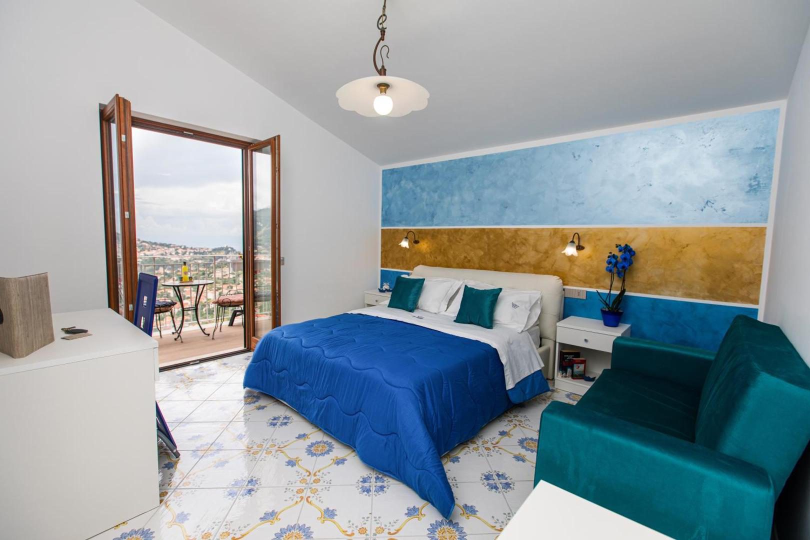 Panariello Palace Agerola – dormitor cu tablie pictata albastru-auriu si balcon cu vedere la vale Panariello Palace Agerola – dormitor cu tablie pictata albastru-auriu si balcon cu vedere la vale