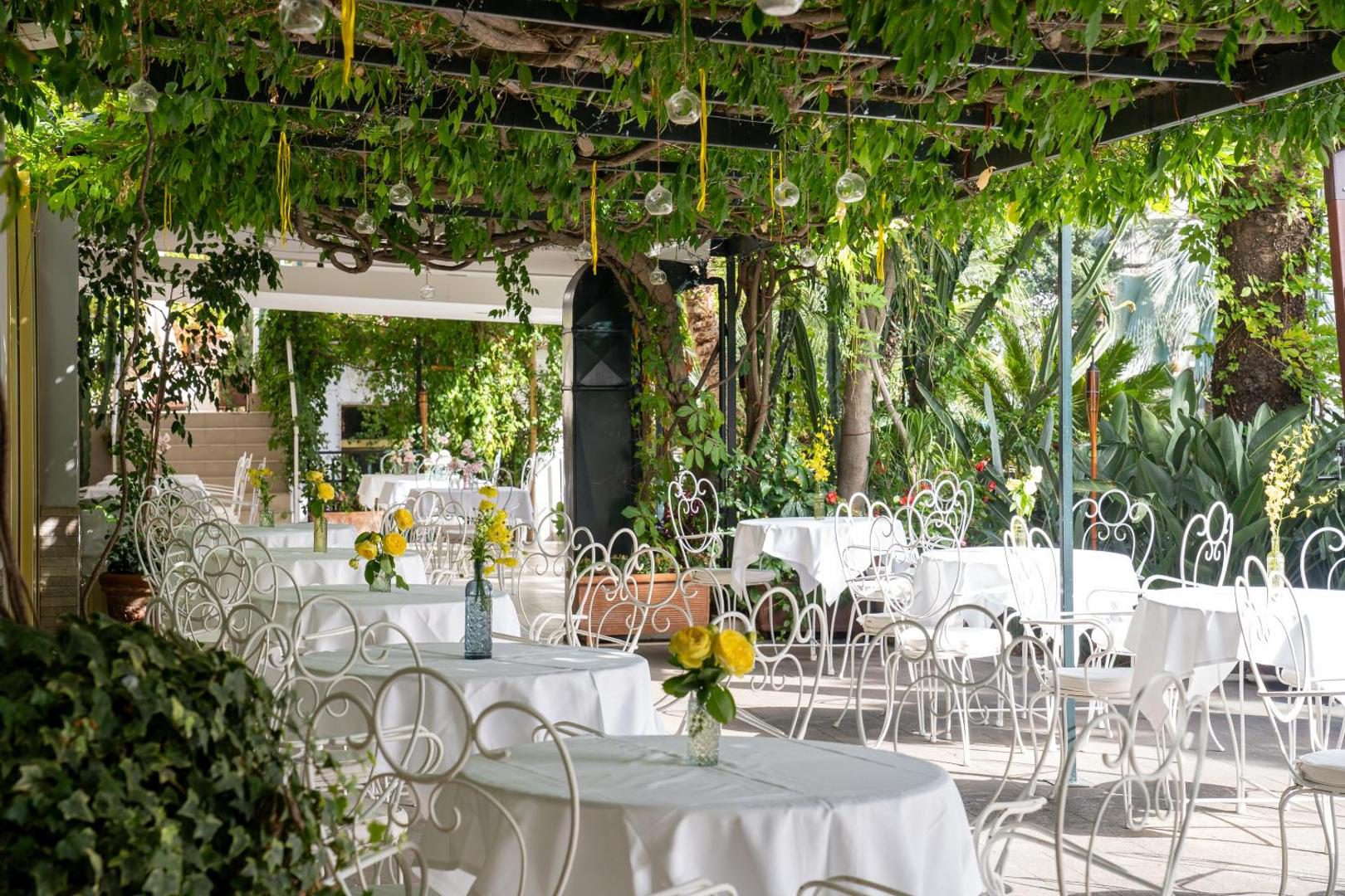 Reginna Palace Hotel Maiori – restaurant in gradina sub pergola verde cu mese albe Reginna Palace Hotel Maiori – restaurant in gradina sub pergola verde cu mese albe
