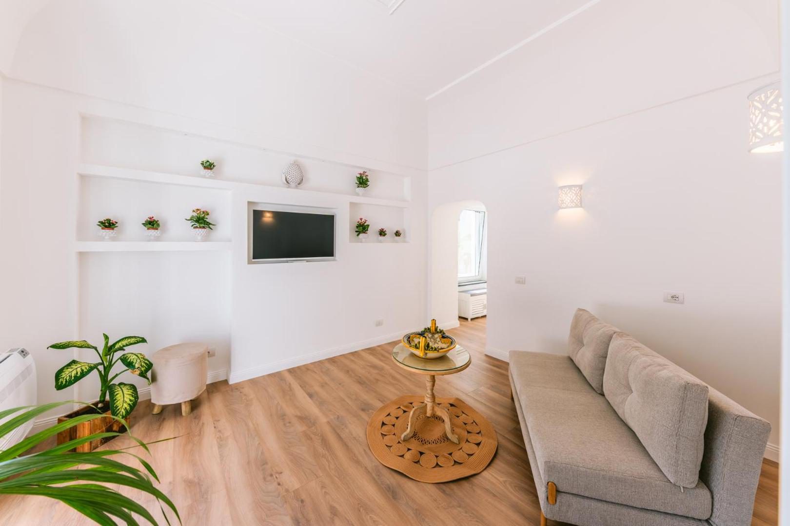 Villa Mary Suites Positano – living luminos cu canapea gri si plante decorative Villa Mary Suites Positano – living luminos cu canapea gri si plante decorative
