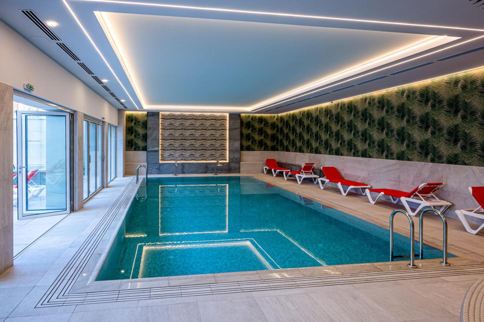 Piscina interioară a Hotel Carolin, cu șezlonguri pe margine Piscina interioară a Hotel Carolin, cu șezlonguri pe margine