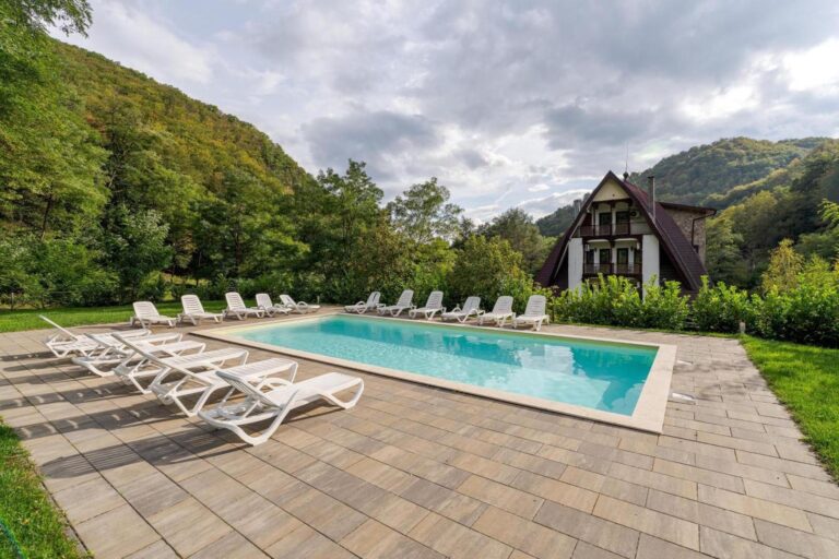 Pension Casa Vanatorilor – piscina exterioară cu șezlonguri, cu pensiunea și dealurile împădurite în fundal